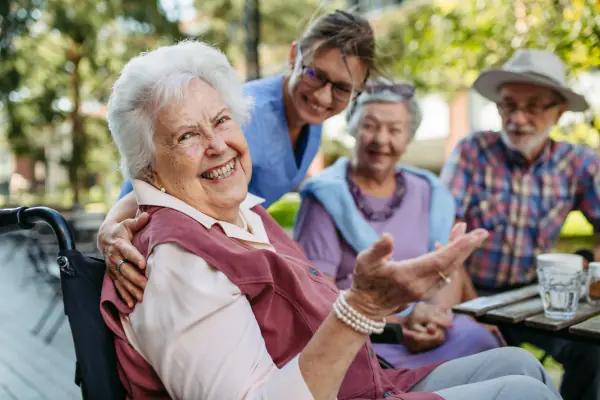 Smiling older adult in a wheelchair enjoying respite care support with companions and a caregiver