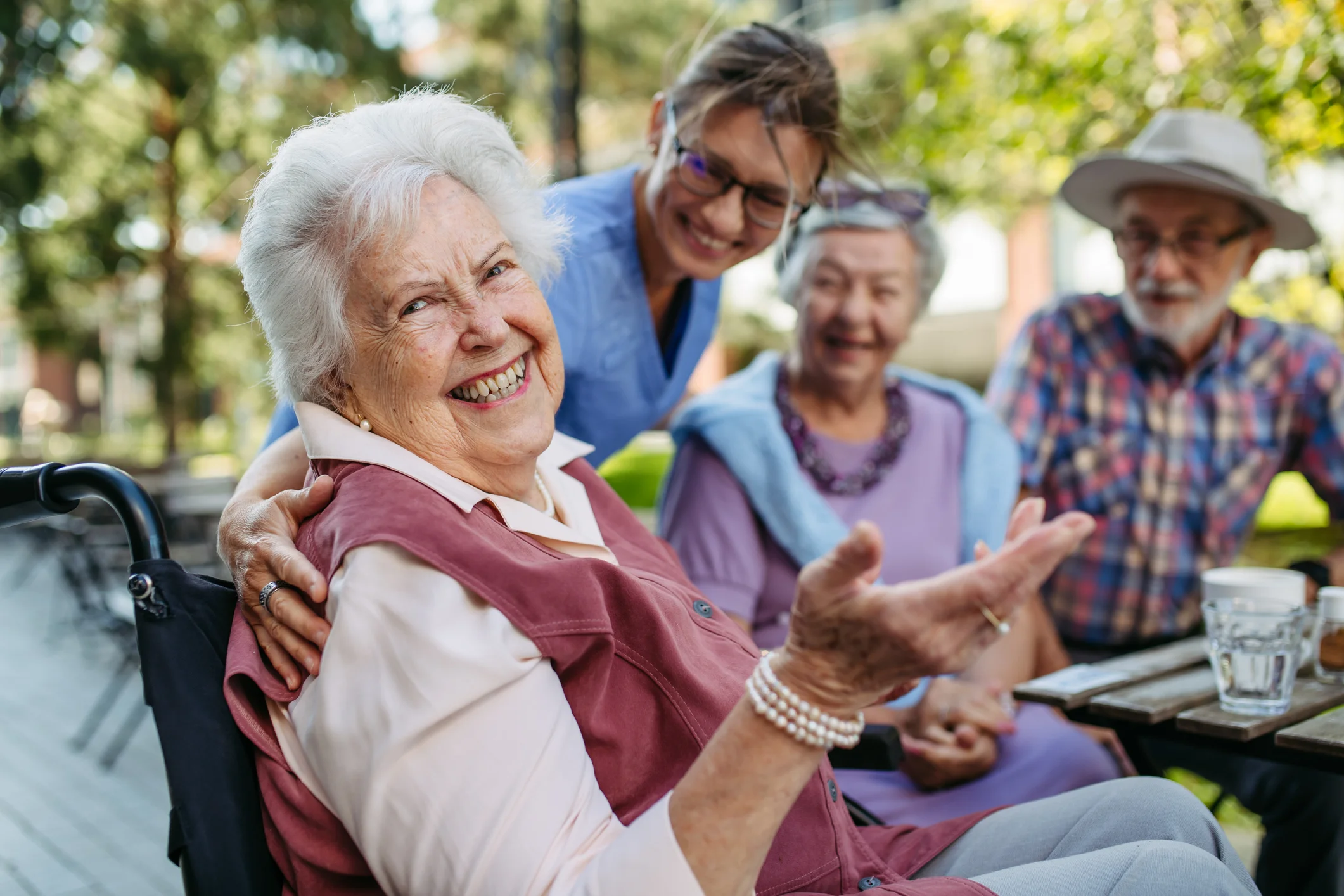 Smiling older adult in a wheelchair enjoying respite care support with companions and a caregiver